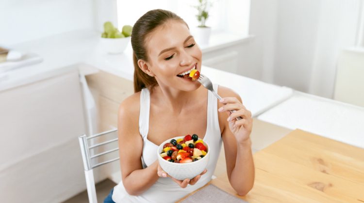 Smiling woman enjoying a fresh fruit salad, highlighting healthy eating tips for maintaining oral health during the holidays in Cupertino, CA.